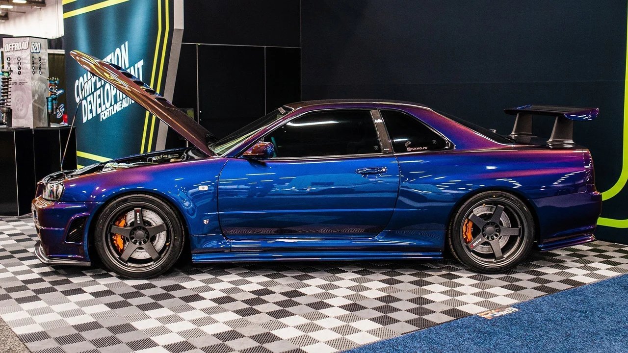 Blue sports car with open hood on a checkered floor, likely at an auto show.