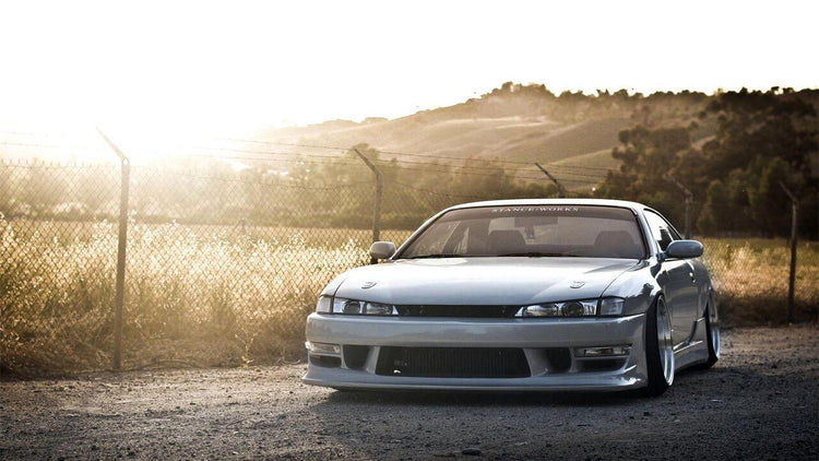A pristine white S14 Silvia 240SX gracefully positioned along the winding country mountain roads on a beautiful day, capturing both the elegance of the vehicle and the serene charm of the surrounding landscape.