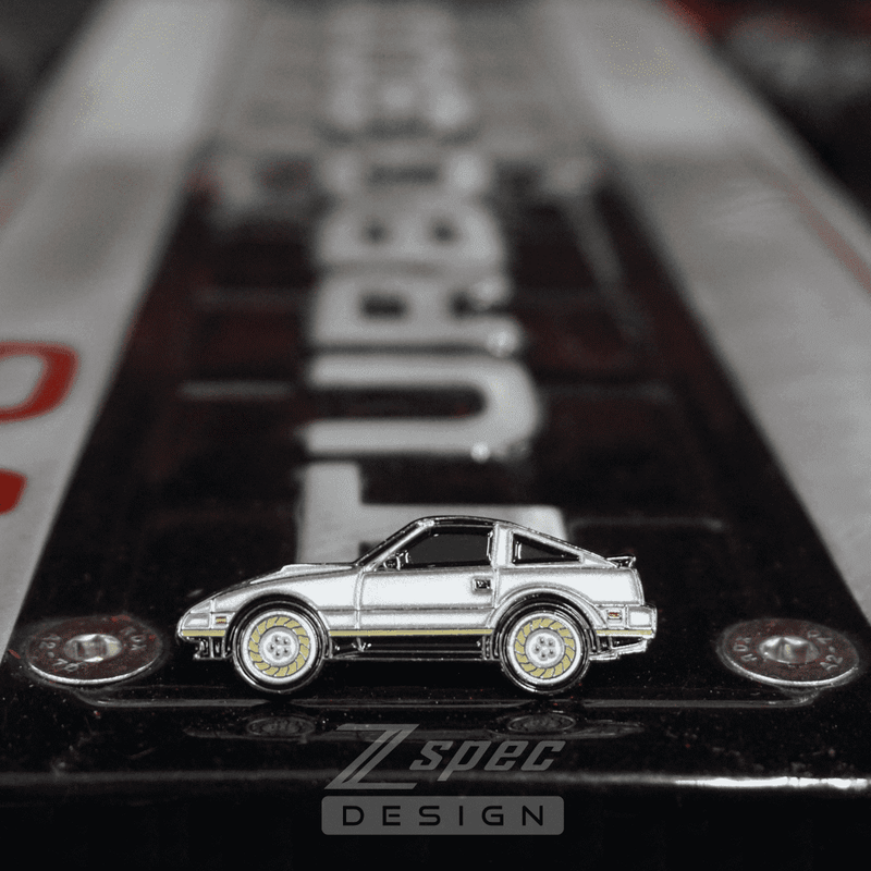 Load image into Gallery viewer, Silver ZSPEC hat pin shaped like a Nissan Z31 300ZX Anniversary Edition car with gold-accented wheels.
