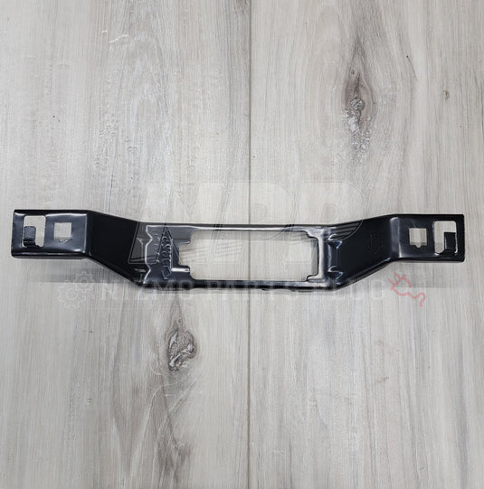 New black license plate lamp bracket for R34 Nissan Skyline on a light wood grain surface.