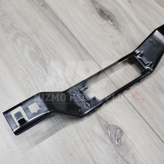 New black Nissan R34 Skyline license plate lamp bracket on a wood background.